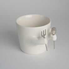 Ceramic mug with sculpted helping hands holding a removable spoon and fork