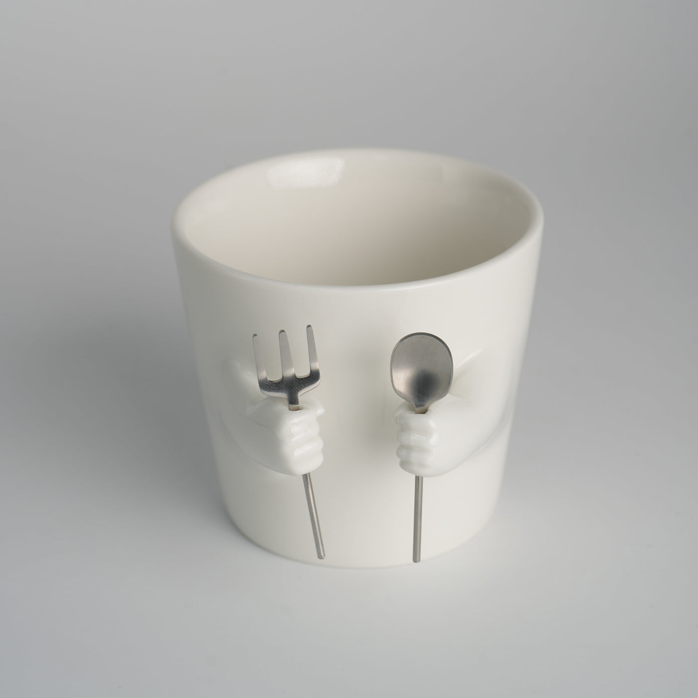 Ceramic mug with sculpted helping hands holding a removable spoon and fork