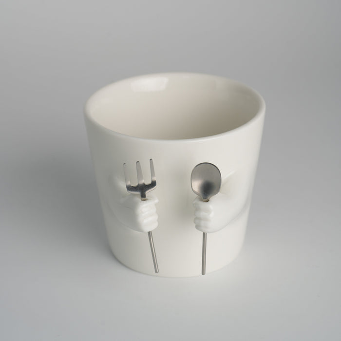 Ceramic mug with sculpted helping hands holding a removable spoon and fork