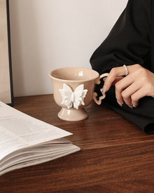 Beige ceramic mug with raised butterfly detail and butterfly-shaped handle