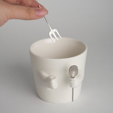 Ceramic mug with sculpted helping hands holding a removable spoon and fork