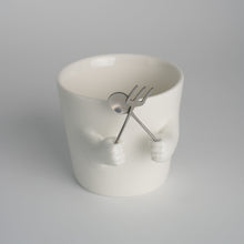Ceramic mug with sculpted helping hands holding a removable spoon and fork